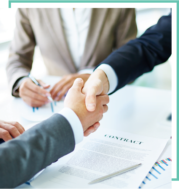 Two people in business attire are shaking hands over a contract on a table, while a third person is holding a pen and taking notes. The scene conveys a business agreement or partnership being made.