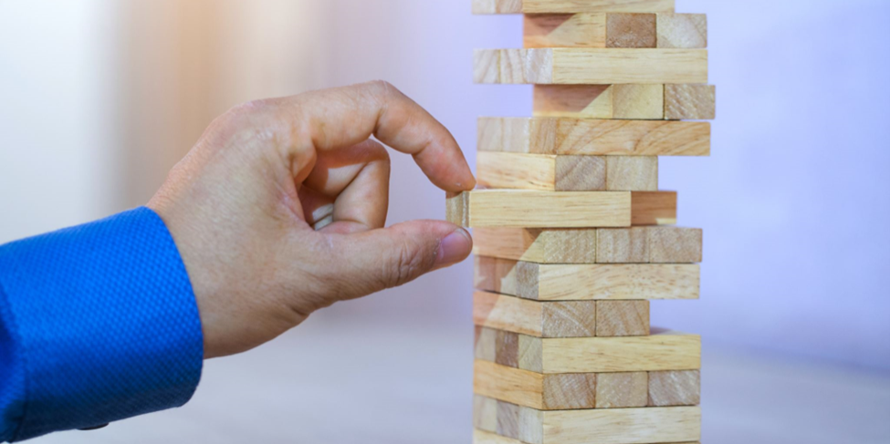 A close-up of a hand in a blue shirt carefully pulling a wooden block from a Jenga tower.